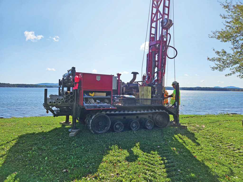 Two men operating a drill rig next to a lake.