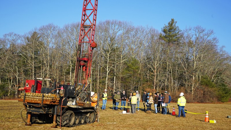 Drill rig with drilling crew and college students in the background