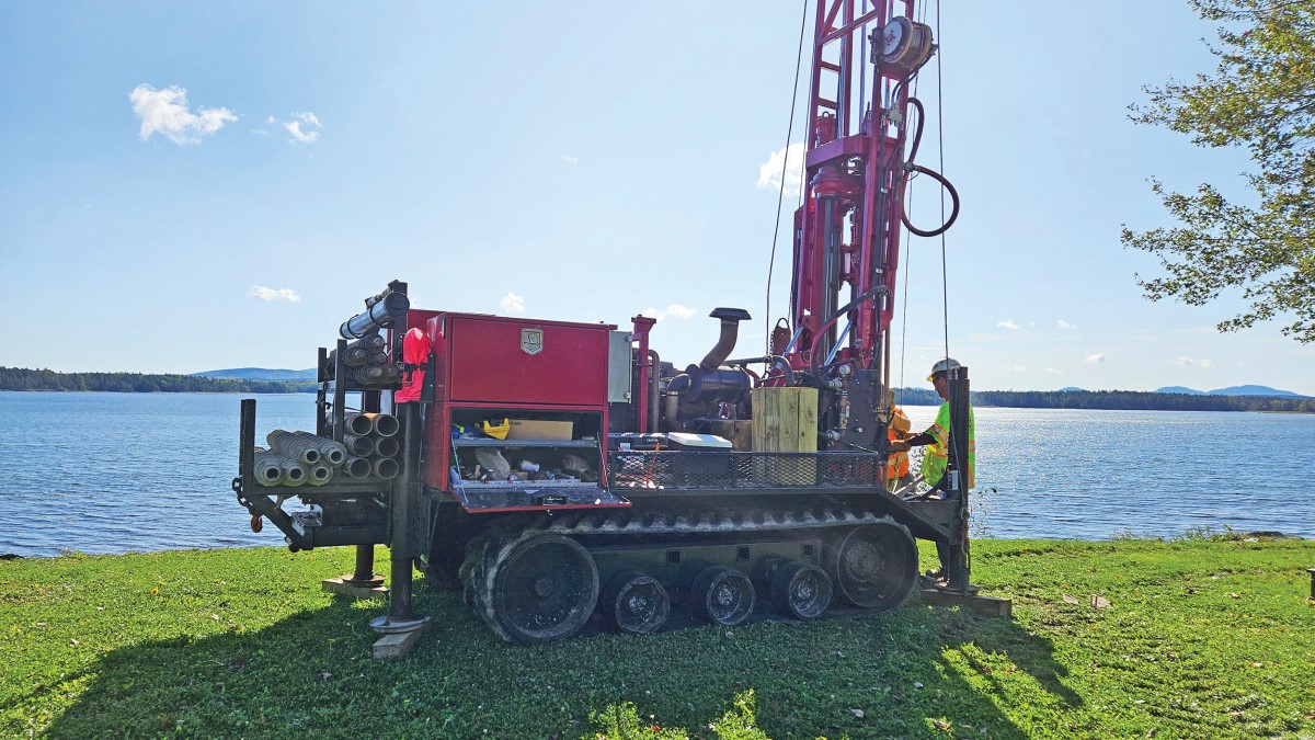 Two men operating a drill rig next to a lake.