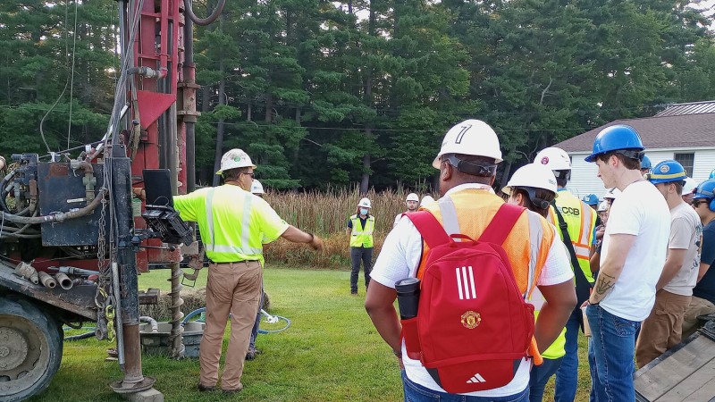 Driller speaking to group of college students during a geotechnical drilling demonstration on campus.