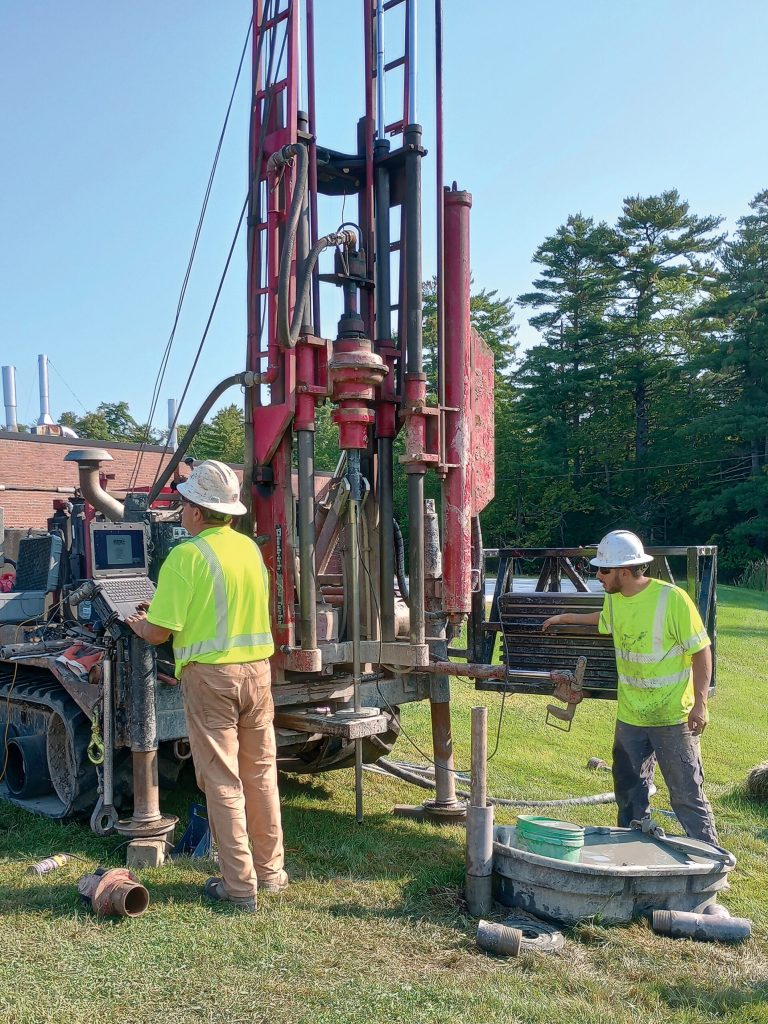 Photo of two men working a drill rig in a field.