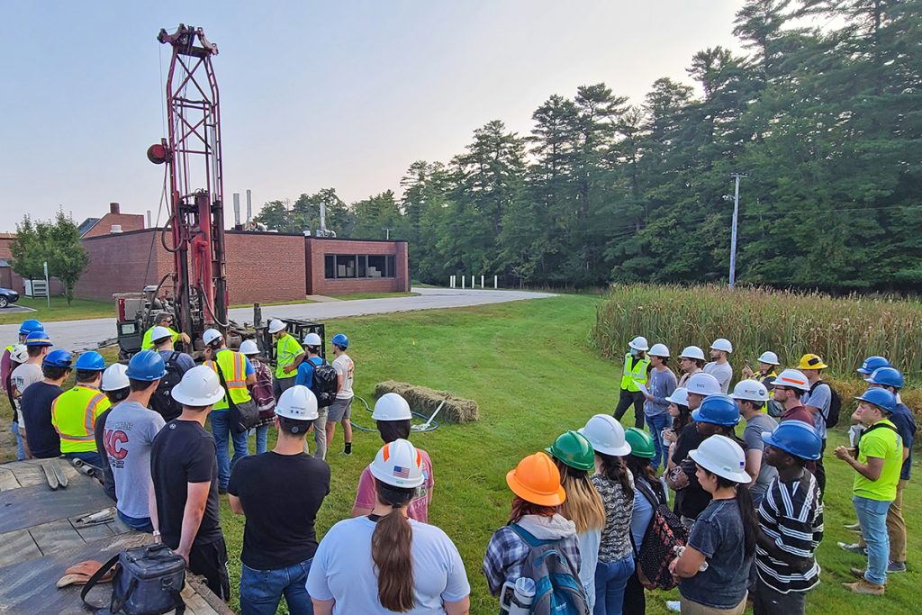 A group of college students look toward drill rig during a geotechnical drilling demonstration on campus.
