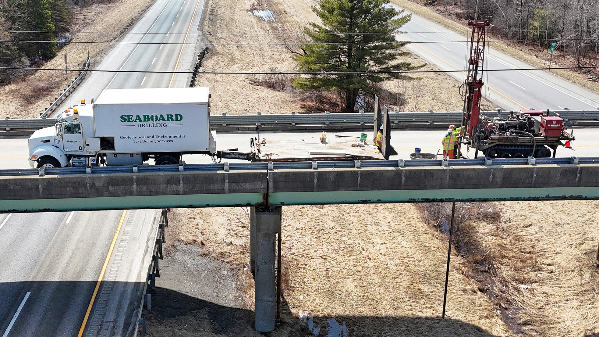 Seaboard drilling box truck and trailer and drill rig on an overpass above the highway.