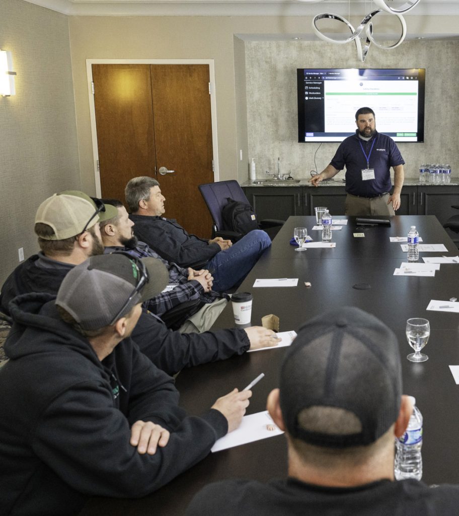 Group of employees around a conference room table with one speaking to the group.